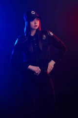 Fototapeta na wymiar Serious female police officer is posing for the camera against a black background with red and blue backlighting.