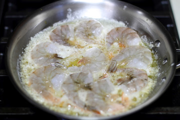 Shrimp scampi cooking in butter and garlic in a stainless steel skillet on the stove.