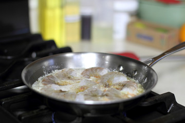 Shrimp scampi cooking in butter and garlic in a stainless steel skillet on the stove.