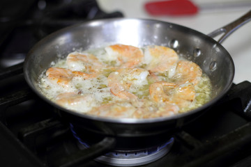 Shrimp scampi cooking in butter and garlic in a stainless steel skillet on the stove.