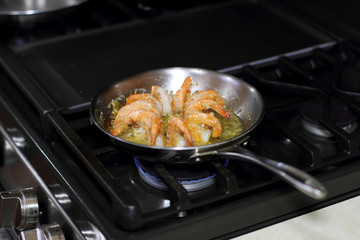 Shrimp scampi cooking in butter and garlic in a stainless steel skillet on the stove.