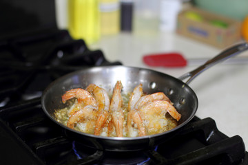 Shrimp scampi cooking in butter and garlic in a stainless steel skillet on the stove.