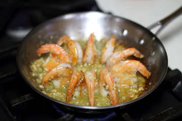 Shrimp scampi cooking in butter and garlic in a stainless steel skillet on the stove.