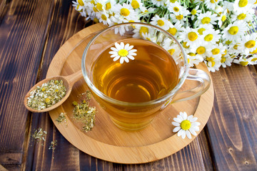 Tea in the glass cup with chamomile on the cutting board  on the brown wooden background