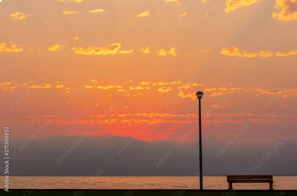 Wall mural lonely street lamp and bench in front of the beautiful bright red sunset