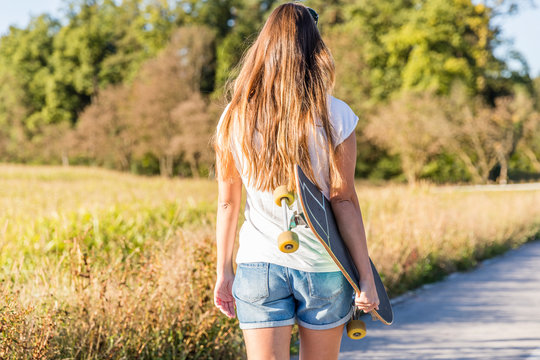 Young beautiful woman walking outdoors with skateboard