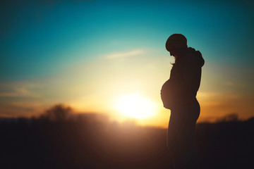 Silhouette of a future mom, pregnant woman relax in the park on a sunset background