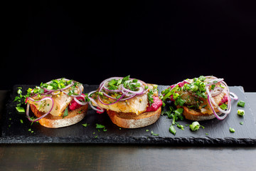 Three smoked salmon sandwich laid out on a black slate.