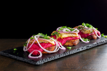 Three smoked salmon sandwich laid out on a black slate.