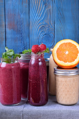 Assortment of different smoothies topped with fruits, berries and mint on the table against the blue background