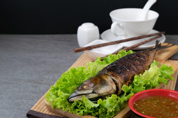Grilled Saba Fish in wooden dish with seafood sauce on table.