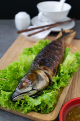 Grilled Saba Fish in wooden dish with seafood sauce on table.