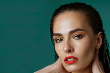 Portrait of a sexy woman with wet black hair and red lips. Professional makeup. Long hair combed up. Look into the camera, brown eyes, close-up on green blue background, copyspase
