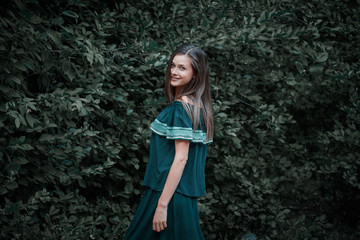 Young beautiful girl with long blond hair stands against the background of foliage, portrait of a cute female outdoors