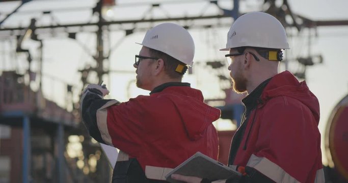 Two engineers at oil factory giving instructrions to truck driver with walkie-talkie