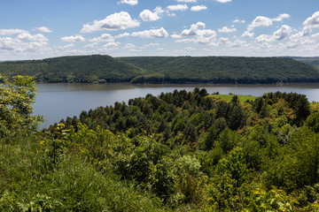 Fototapeta na wymiar The narrow strip of water of the Dniester River is clamped between the high hills of the shores covered with green forest. Summer landscape. Ukraine.