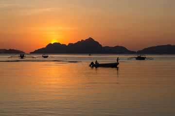 Silhouettes of boats in tropical harbor in evening. Sunset in lagoon in Philippines, Palawan, El Nido. Sunset on beach. Scenic sunset with mountains isles on horizon. Summer vacation and travel. 