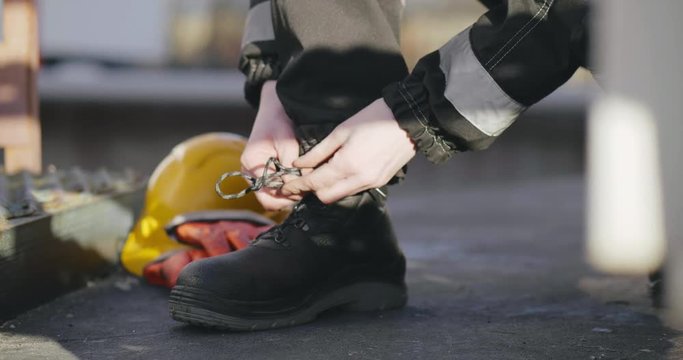 Engineer ties laces on work shoes while working at factory