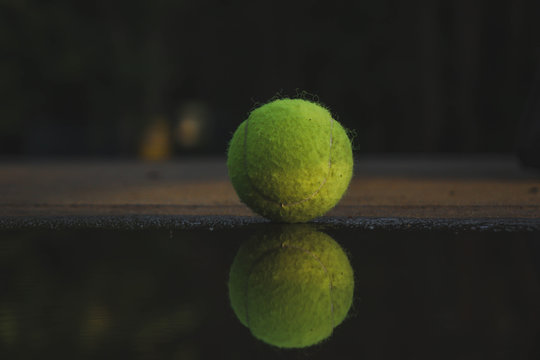 the tennis ball is near the puddle, the ball is reflected in the water
