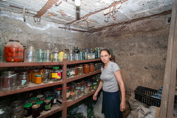 The woman in the cellar is gray-haired, the girl prepares food for the winter, canned food in glass jars on the rack.