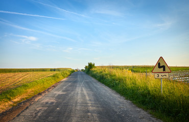 Picture of a country road with dangerous bends traffic sign at sunset.