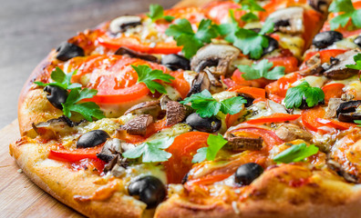 sliced Pizza with Mozzarella cheese, Tomatoes, pepper, olive, mushrooms, Spices and Fresh leaf. Italian pizza on wooden table background