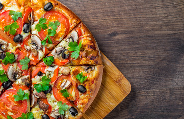 sliced Pizza with Mozzarella cheese, Tomatoes, pepper, olive, mushrooms, Spices and Fresh leaf. Italian pizza on wooden table background