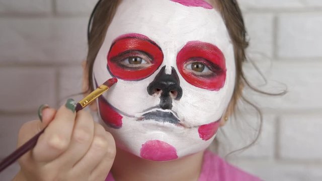 Child draws face for Halloween. Sad clown. A cute little girl paints her face for halloween.