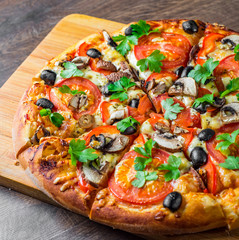 sliced Pizza with Mozzarella cheese, Tomatoes, pepper, olive, mushrooms, Spices and Fresh leaf. Italian pizza on wooden table background