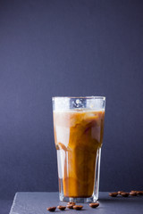 Iced coffee with milk on a dark background. Summer drink with caffeine on the slate board. Latte in a glass cup and coffee beans. Copy space