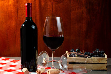 Bottle of red wine in wine cellar for tasting. Red wooden background with wooden box with grapes....