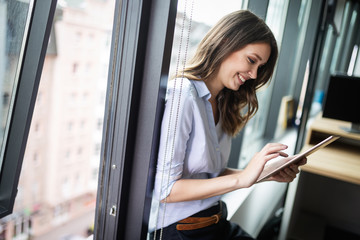 Happy woman manager holding tablet and standing in modern office