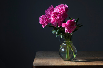 bouquet of pink peonies in a transparent vase on a dark background