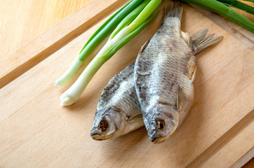 Dried fish and green onion on the table. Salty dry river fish on a wooden background