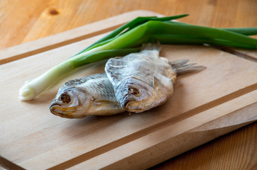 Dried fish and green onion on the table. Salty dry river fish on a wooden background
