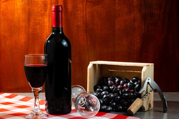 Bottle of red wine in wine cellar for tasting. Red wooden background with wooden box with grapes....