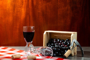 Bottle of red wine in wine cellar for tasting. Red wooden background with wooden box with grapes. Wine tradition and culture concept.