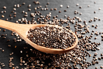 Chia in wooden spoon on a dark background slate plate. Top view.