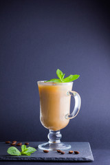 Iced coffee with milk on a dark background. Latte and fresh mint on a slate board. Summer drink in a glass, and coffee beans. Copy space