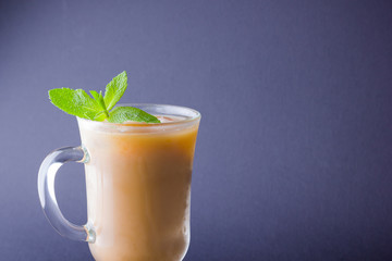 Iced coffee with milk on a dark background. Latte and fresh mint on a slate board. Summer drink in a glass, and coffee beans. Copy space