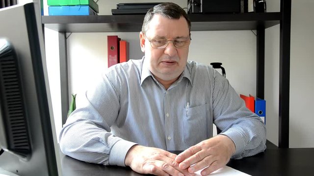 Middle aged man sitting at the desk breathes into a brown paper bag as a remedy for panic attack