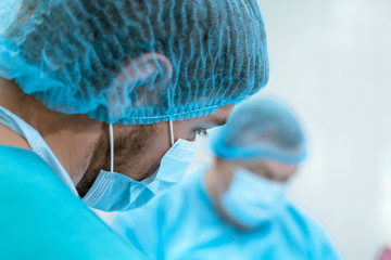 An experienced surgeon in a mask and gown operates in a sterile operating room with an assistant...