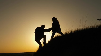 woman traveler stretches hand to man climbing to the top of a hill. travelers climb the cliff holding hands. teamwork of business people. Happy family on vacation. tourists hug on top of mountain