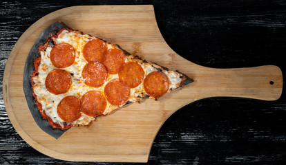 A slice of margarita pizza, on black dough. Lies on a wooden platform.