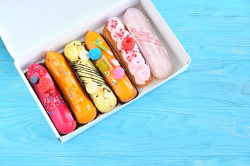 Delicious french eclairs set with original cream decor and fresh berries in white box on blue wooden background. Selective focus. Tasty dessert profiteroles with colorful sugar elements and raspberry