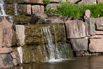 City Park "Karhula" Finland Kotka city. Waterfall, water flows over granite stones. Dribbled lynx sculpture. Colorful photo of a park landscape.