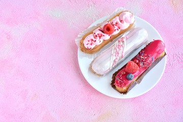 Tasty French eclairs cake with creative pink decor and fresh berries on pink textured table. Selective focus. Delicious dessert profiteroles with pink and red icing and sugar decor elements. 