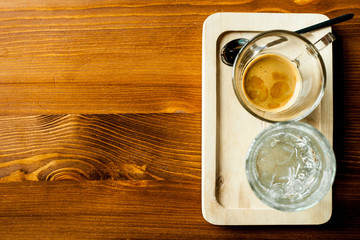 Strong black coffee in a transparent mug, served with a glass of water, on a wooden tray, on a wooden background with a place for the inscription. The concept of Breakfast.