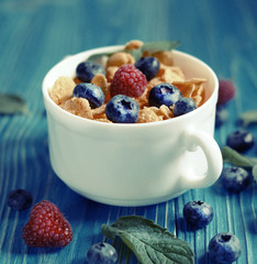 Healthy eating, food and diet concept - Cornflakes with berries raspberries and blueberries on blue wooden background.