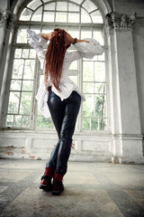dreadlocks fashionable girl dressed in white shirt and black leather trousers posing in font of old...